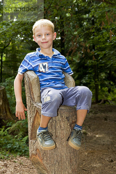 Ein Junge  6 Jahre  sitzt auf einem zum Thron geschnitzten Baumstamm