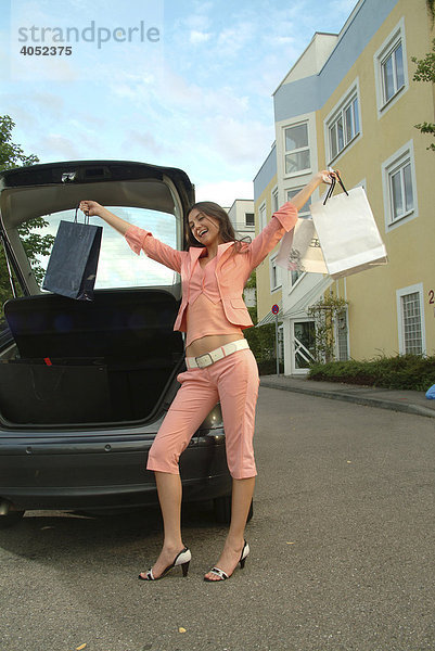 Junge Frau in einem rosa Anzug holt ihre Einkaufstüten aus dem Kofferraum ihres Autos