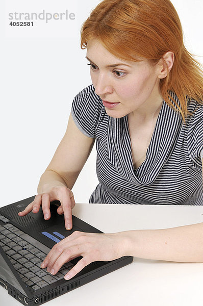 Rothaarige  attraktive Frau mit Laptop am Tisch  arbeitet konzentriert  surft  Internet