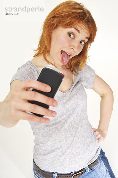 Rothaarige  attraktive Frau macht Foto mit Handy  streckt Zunge heraus  frech