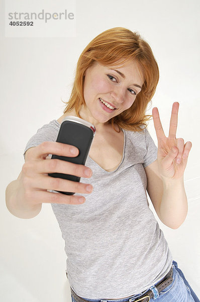 Rothaarige  attraktive Frau macht Foto mit Handy  macht Peace Zeichen