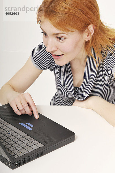 Rothaarige  attraktive Frau mit Laptop am Tisch  arbeitet konzentriert  surft  Internet  fröhlich  überrascht