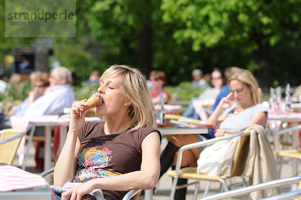 Junge blonde Frau sitzt in einem Café im Sonnenschein  isst ein Eis  sonnt sich  entspannt
