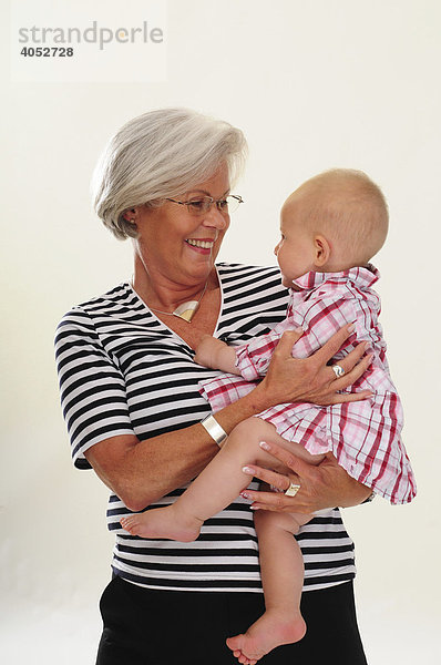 Portrait sympathische Frau  60  Seniorin  mit grauen Haaren hat Enkeltochter  Baby auf dem Arm