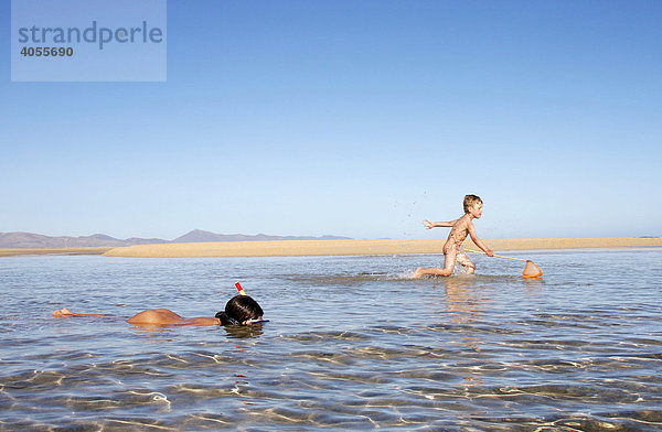 Junge  4 Jahre  versucht mit dem Netz Fische zu fangen  Mädchen  8 Jahre  unternimmt im seichten Wasser erste Schnorchelversuche  am Strand von Fuerteventura  Kanarische Insel  Spanien  Europa