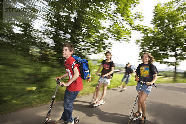 Schulkinder  Jungen und Mädchen  fahren mit dem Trottinett  Roller  Scooter  Kickboard auf dem Schulweg  Basel  Schweiz  Europa