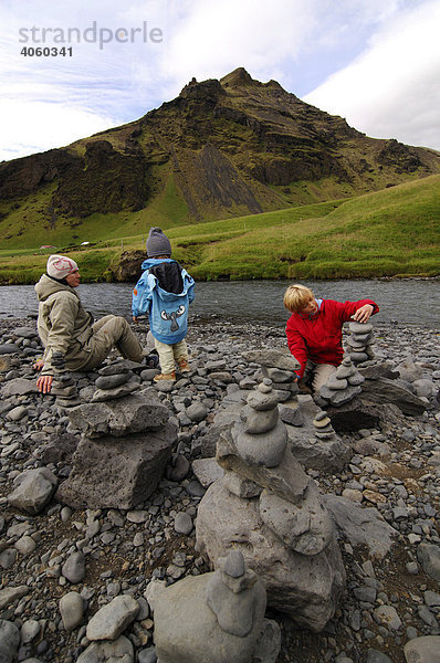 Frau und zwei Kinder bauen Steinmänner am Skogafoss  Island  Europa