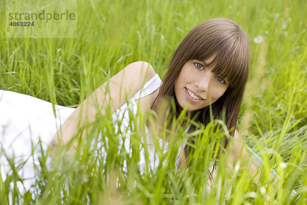 Junge dunkelhaarige Frau mit weißem Kleid genießt auf einer grünen Wiese liegend den Sommer