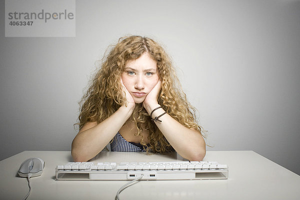 Junge langhaarige Frau sitzt frustriert vor einer Computertastatur am Tisch