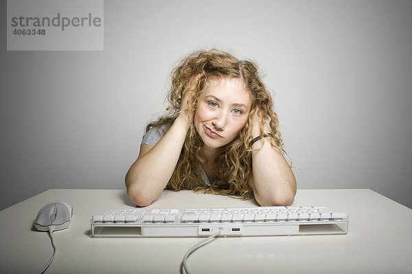 Junge langhaarige Frau sitzt frustriert vor einer Computertastatur am Tisch