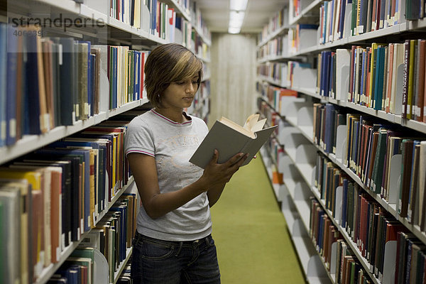 Junge dunkelhaarige Frau  Studentin  blättert in einem Buch zwischen den Bücherregalen in der Bibliothek