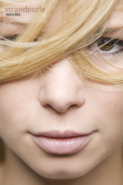Nahaufnahme des Gesichts einer jungen blonden Frau mit in das Gesicht gewehten Haarsträhnen