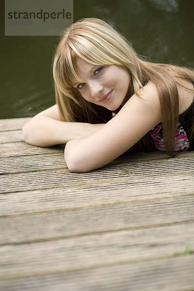 Junge blonde Frau liegt auf einem Steg am Wasser