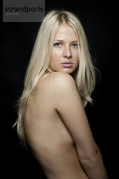 Junge blonde Frau mit freiem Oberkörper verdeckt mit ihren Armen die Brust