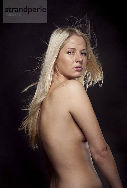 Junge blonde Frau mit freiem Oberkörper verdeckt mit ihren Armen die Brust