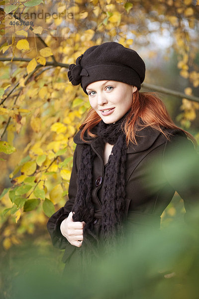 Junge rothaarige Frau mit Mütze und Schal im herbstlichen Wald