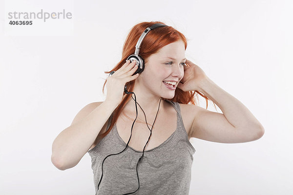 Junge Frau mit langen roten Haaren hört Musik über Kopfhörer