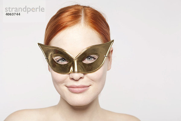 Junge rothaarige Frau mit goldfarbener Maske