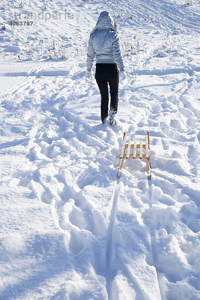 Junge Frau zieht im Schnee einen Schlitten hinter sich her
