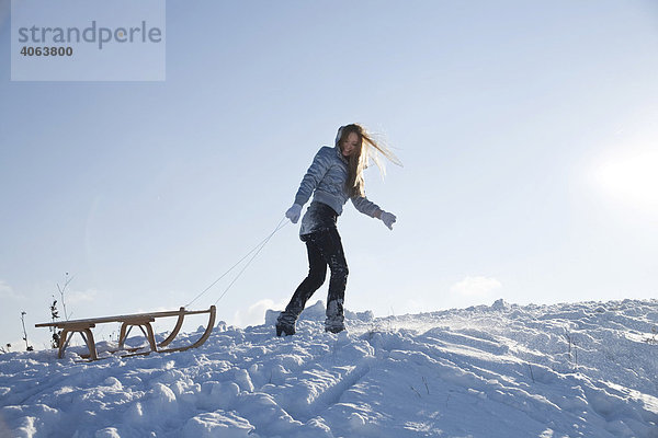 Junge Frau zieht im Schnee einen Schlitten hinter sich her