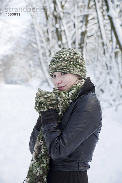 Portrait einer frierenden jungen Frau mit Mütze und Handschuhen in einer Schneelandschaft