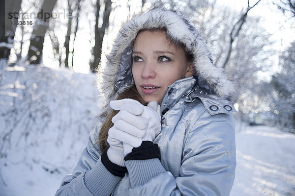 Portrait einer frierenden jungen Frau mit Mütze und Handschuhen in einer Schneelandschaft
