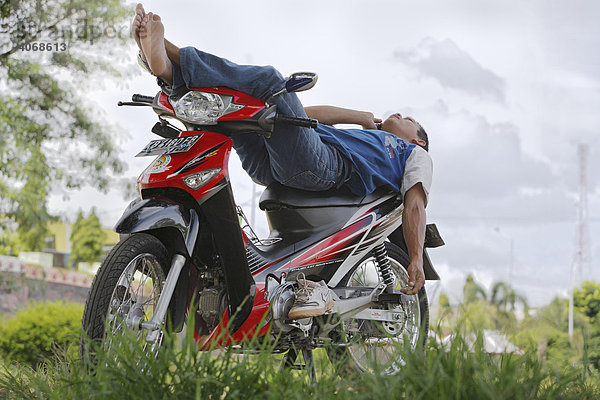 Junger Mann liegt auf Moped  telefoniert mit Handy  Putussibau  West-Kalimantan  Borneo  Indonesien  Asien