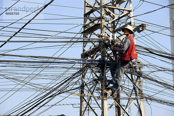 Elektrifizierung ohne Arbeitsschutz  Elektriker hängt im Gewirr von Stromkabeln  Vientiane  Laos  Asien