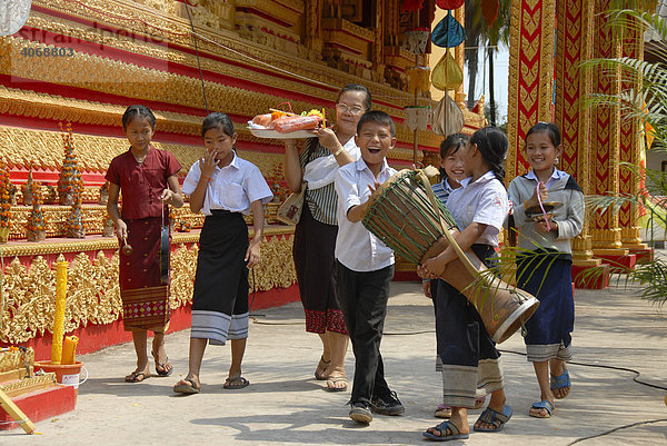 Gläubige buddhistische Familie mit Kindern beim freudigen Gang um den Tempel mit Trommel und Opferschale  Vientiane  Laos  Südostasien
