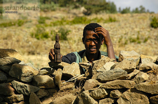 Junge hinter einer Mauer mit einer heiligen Figur in der Hand  Axum  Äthiopien  Afrika