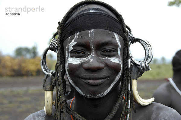 Portrait  junger Mann vom Volk der Mursi lächelt mit wildem  schwerem Kopfschmuck aus Hauern  bei Jinka  Äthiopien  Afrika