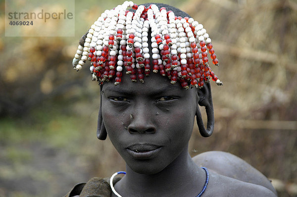 Portrait  junge Frau vom Volk der Mursi mit buntem Kopfschmuck und weit geweiteten Ohrläppchen  bei Jinka  Äthiopien  Afrika