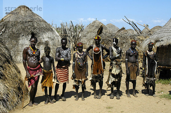 Gruppe von wild gekleideten und bunt geschmückten Menschen in ihrem Dorf aus Strohhütten  Volk der Karo  Kolcho  Südliches Omo Tal  Äthiopien  Afrika