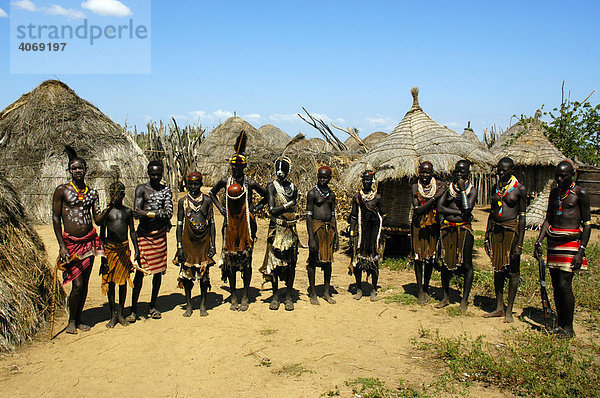 Gruppe von wild gekleideten und bunt geschmückten Menschen in ihrem Dorf aus Strohhütten  Volk der Karo  Kolcho  Südliches Omo-Tal  Äthiopien  Ostafrika  Afrika