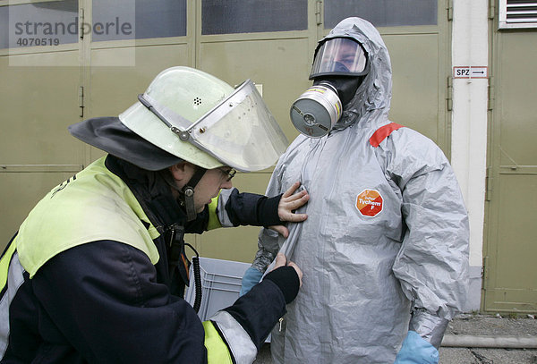 Feuerwehrmann hilft seinem Kollegen beim Anlegen eines Schutzanzugs bei einer Katastrophenschutzübung bei Poing  Bayern  Deutschland  Europa