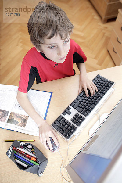 Ein Junge  10 Jahre alt  sitzt vor einem Computer und macht seine Hausaufgaben