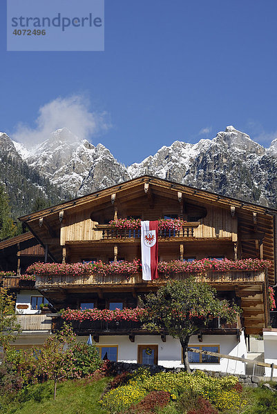 Mit Blumen und Tirolfahne geschmücktes Haus in den Tiroler Alpen  hinten verschneites Bergmassiv  Alpbach  Tirol  Österreich  Europa