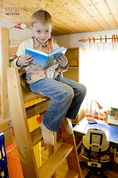 Ein Junge  6 Jahre  sitzt auf einer Bettleiter und liest in einer Kinderbibel