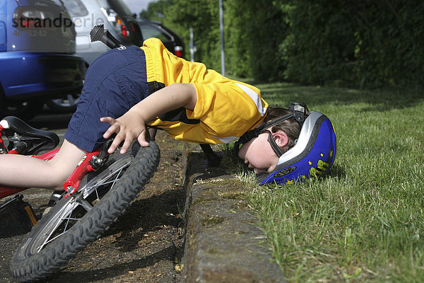 Fünfjähriger Junge trägt einen Fahrradhelm und stürzt vom Rad  gestellte Szene