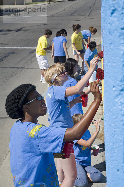 Freiwillige im Summer in the City Program malen eine Wandmalerei auf eine Mauer nahe des Detroit's Eastern Farmers Market Wochenmarkts  Detroit  Michigan  USA