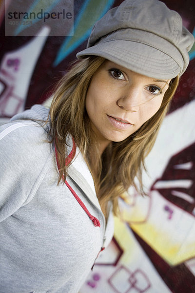 Portrait einer Frau mit Mütze vor einer Graffiti-Wand