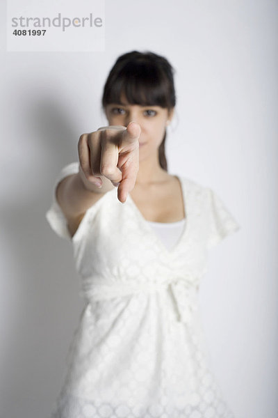 Junge Frau mit weißem Oberteil zeigt mit dem Finger auf den Betrachter