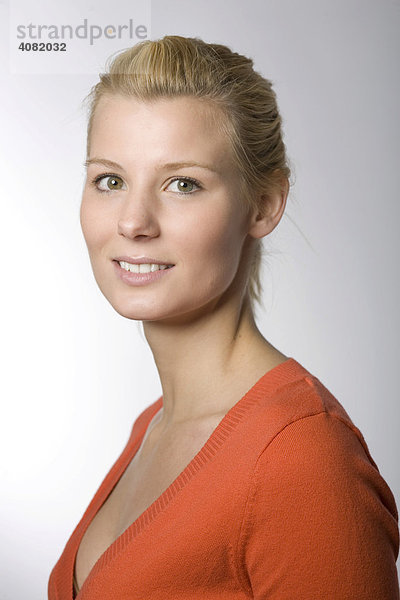 Portrait einer lächelnden jungen Frau im orangenen Pullover