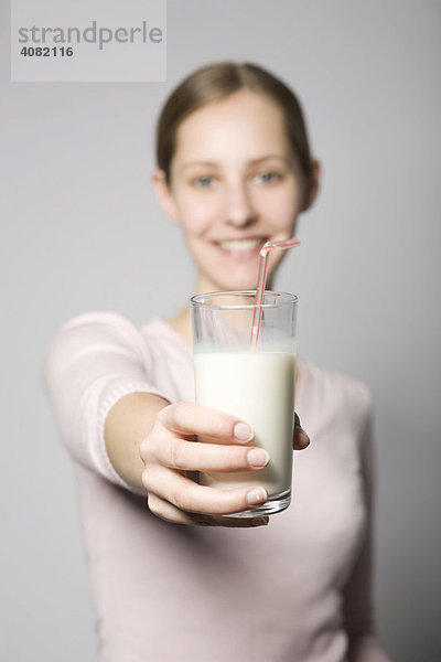 Junge Frau hält ein Glas Milch in Richtung Kamera