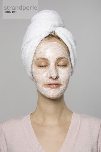 Junge Frau mit Gesichtsmaske und weißem Handtuch