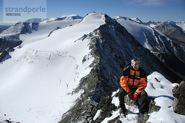 Bergsteiger sitzt auf Felsen vorschneebedecktem Berg Kharkhiraa Mongolischer Altai bei Ulaangom Uvs Aimag Mongolei