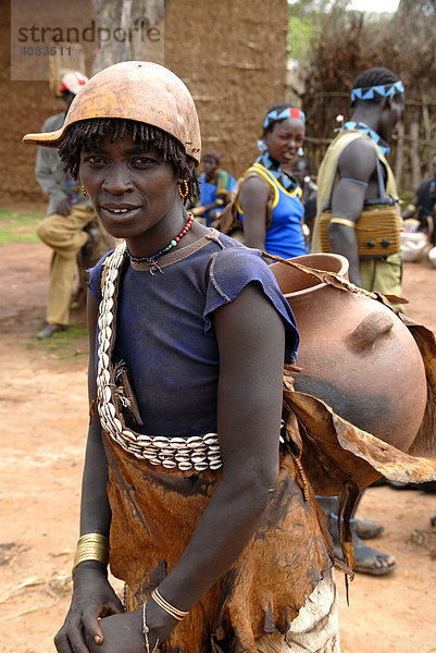 Frau mit Kette aus Kaurimuscheln und Kalabasse auf dem Kopf trägt einen großen Tontopf auf dem Rücken auf dem Markt von Keyafer Äthiopien