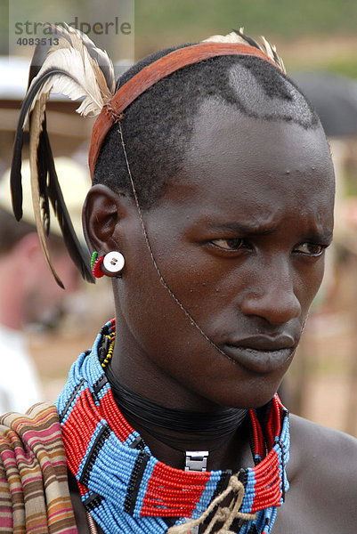 Portrait Junger Mann vom Volk der Banna mit Federn als Kopfschmuck und bunter Halskette auf dem Markt von Keyafer Äthiopien