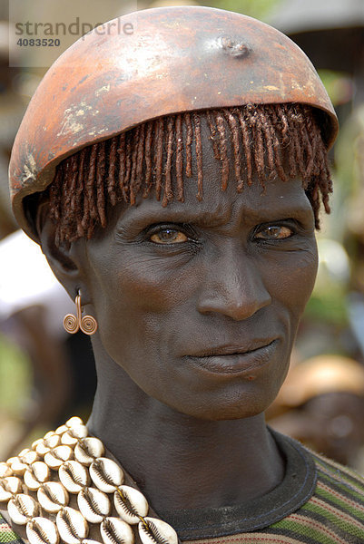 Portrait streng dreinblickende Frau mit Kette aus Kaurimuscheln und Kalabasse auf dem Kopf auf dem Markt von Keyafer Äthiopien