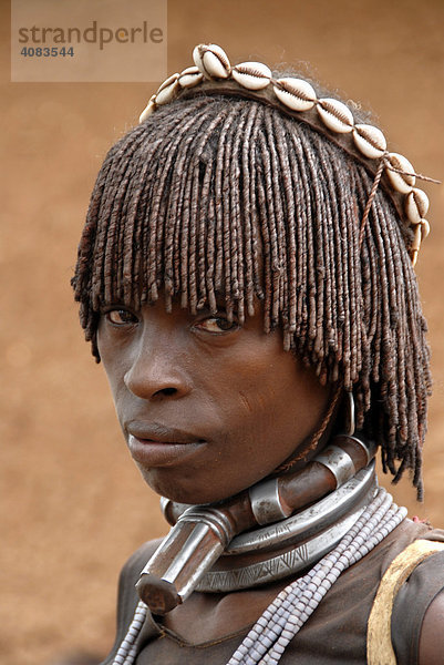 Portrait Frau vom Volk der Hamar schaut traurig und trägt typische Lehm Haarfrisur und Ketten aus Metall und Kaurimuscheln auf dem Markt von Dimeka Äthiopien